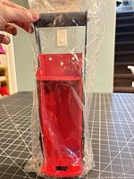 Front view of can crusher sealed in plastic showing red body and black handle