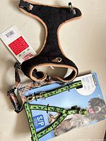 Both harnesses laid out: plaid fleece-padded harness and green patterned nylon harness on retail card