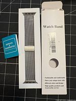 Silver stainless steel mesh watch band in tray inside white retail box with blue service guarantee card