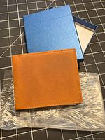 wallet exterior resting on plastic sleeve beside open blue gift box