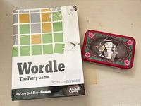 Front view of sealed Wordle game beside closed decorative tin