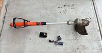 Full view of trimmer with battery and charger on concrete surface