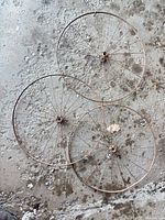 Three rusty 20 inch bicycle wheels with hubs and spokes on concrete floor