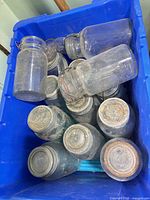 Bin containing multiple clear glass canning jars with assorted lids and closures