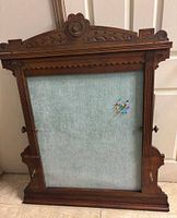 Full front view of carved wood bulletin board showing frame, fabric panel, side knobs and hooks