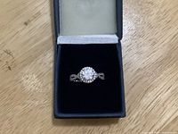 Ring top view showing round centre stone, halo and split shank in presentation box