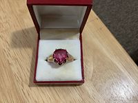 Ring in open red presentation box, top view showing heart-shaped pink stone and gold band