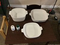 Three square Corning Ware casserole dishes and two Gemco shakers displayed on table