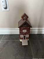 Front view of painted concrete schoolhouse doorstop showing windows, door, steps, bell tower