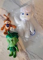 Green Giant Little Sprout plastic figure, Nesquik bunny plush, sealed Pillsbury Doughboy plush displayed together on marble surface
