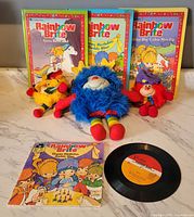 All lot contents laid out: three hardcovers, one softcover book with record, three plush sprites