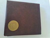 Closed brown coin album with gold-tone medallion on cover