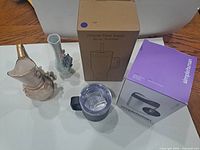 Group shot of all five items including boxed tumbler, boxed receptacle, Yeti mug, and two ceramic vases