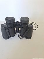 Front view of binoculars showing textured barrels, attached neck strap and lens caps