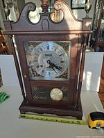 Front view showing entire clock, dial, pendulum, finials, and tape measure for width