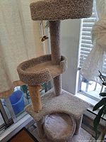 Full view of beige carpet multi-tier cat tree showing cubby base, two posts, middle and top perches, hanging toy