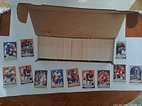Open long cardboard box filled with tightly packed football cards, sample cards displayed below