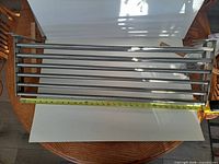 Pair of stainless steel Grundtal shelves laid flat with tape measure showing width around 31.5 inches.