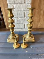 Front view showing two tall and two small brass candlesticks on surface