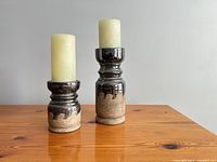 Two ceramic candle holders with pillar candles on wooden surface