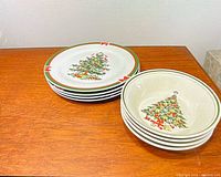 Stack of four dinner plates and four bowls showing matching Christmas tree pattern and rim detailing