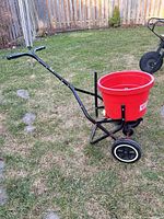 Black-frame spreader side view showing handle, hopper and wheels