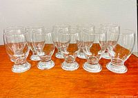 All ten clear footed glasses lined up showing uniform design and condition