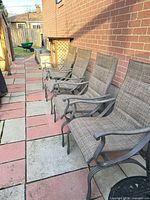 Four stationary sling armchairs lined beside brick wall on patio