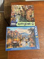 Front view of both sealed 1000-piece puzzle boxes