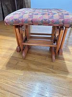 Top and underside view of upholstered glider stool showing geometric patterned cushion and light wood glider frame