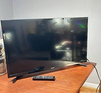 Front view of Samsung 32-inch TV on stand with remote in foreground