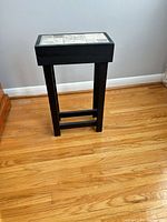 Full view of the narrow black wood end table showing legs, stretcher, and tile top
