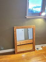 Front view of rectangular mirror with natural wood frame leaning against wall
