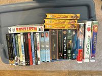 Top view of storage bin containing DVDs and VHS tapes showing visible titles and quantities