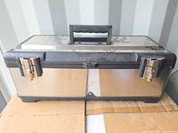 Closed toolbox showing stainless sides, black lid, handle and latches