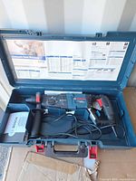 Drill, handle, cord, paperwork in open Bosch case