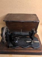 Full view of Singer hand-crank sewing machine on wooden base with cover behind