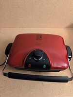 Closed red George Foreman electric grill, front controls visible