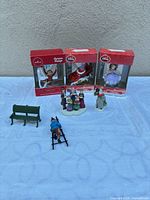Group shot showing three boxed ornaments, caroler figurine, bench, ladder with figure