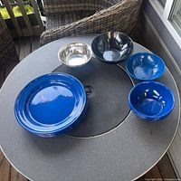 Stacked blue speckled enamel plates, stainless bowl, composite and plastic bowls on table