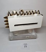 Front-left view showing white rectangular body, gold cone mane, slot mouth, cylindrical legs on acrylic base