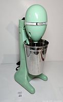 Front view of mint green Hamilton Beach Classic drink mixer with stainless steel cup attached