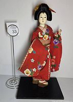 Front view of geisha doll in red floral kimono standing on black base