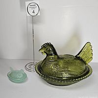 Large and miniature pressed glass hen on nest dishes side by side showing scale and color