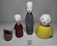 Front view of three monk figurines and bucket