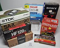 Assorted sealed audio cassette boxes, Memorex cassettes, Maxell DVD-R spindle and Sony VHS tape