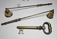 Two brass candle snuffers and brass key letter opener on white background
