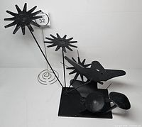 Front view of black metal sculpture with flowers, mushrooms, butterflies on base
