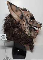 Left side profile of full-head wolf mask on stand showing sculpted face, ear, and fur