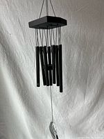 Full view of black wind chime hanging, showing square cap, tubes, striker, and sail